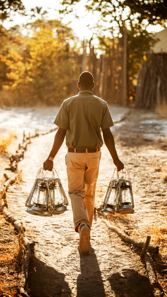 down to earth luxury safari staff carrying kerosene lanterns at sunset in African bush camp