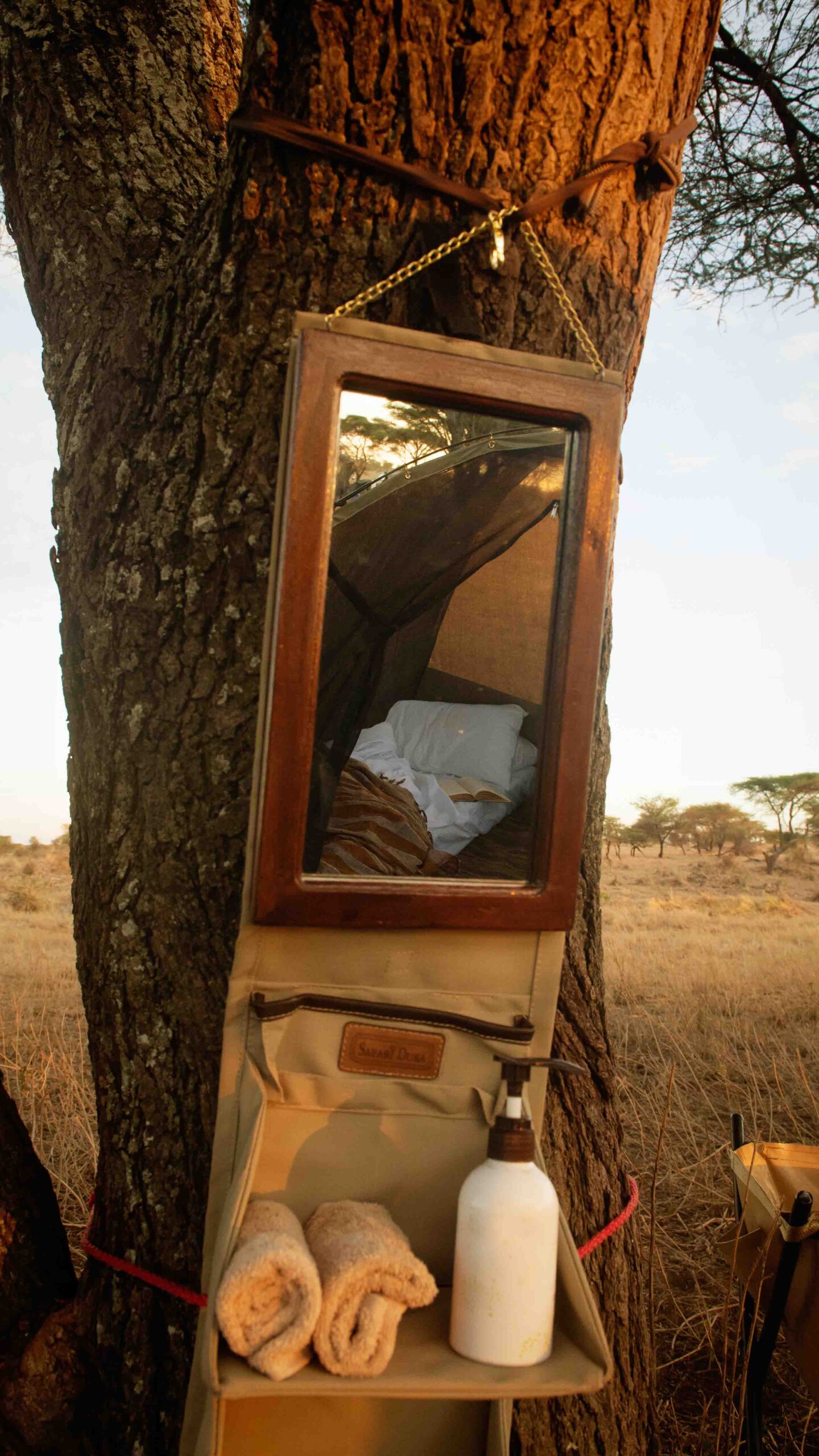 down to earth luxury safari bush bathroom with mirror and safari toiletry bag hanging in tree